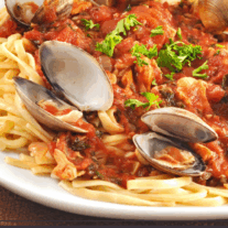 A plate of linguine topped with red clam sauce and fresh clams, garnished with parsley.