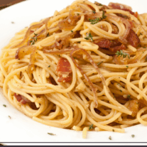 A bowl of spaghetti topped with a savory bacon and onion mixture seasoned with thyme.
