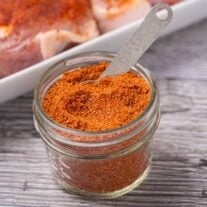 Homemade dry rub for pork chops in a glass jar with measuring spoon.