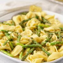 A plate with delicate cheese tortellini tossed with asparagus spears.
