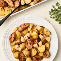 Top-down view of a rustic sheet pan and plate filled with roasted chicken sausage, Granny Smith apples, and baby potatoes, an easy recipe perfect for busy weeknights.