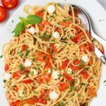 An oval serving platter of caprese pasta; linguine tossed with chopped fresh tomatoes, fresh mozzarella, basil, and parsley.