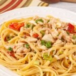 A close view of linguine tossed with crab meat, diced tomatoes, and scallions with serving spoon and towel in the background.