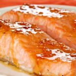 A white serving plate with two oven-roasted salmon fillets topped with orange marmalade and bourbon glaze.