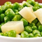 A serving dish filled with buttered green peas and chunks of boiled parsnips.