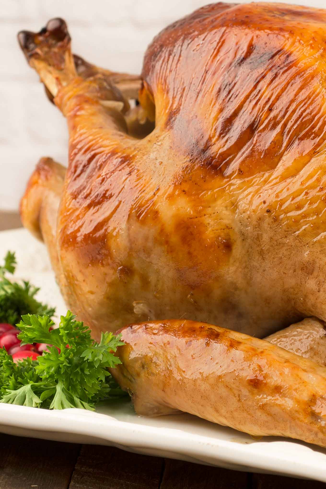 Close-up photo of a whole brined and roasted turkey on a serving platter, garnished with fresh parsley and cranberries.