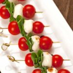 A serving plate of skewered cherry tomatoes, basil leaves, and fresh mozzarella.