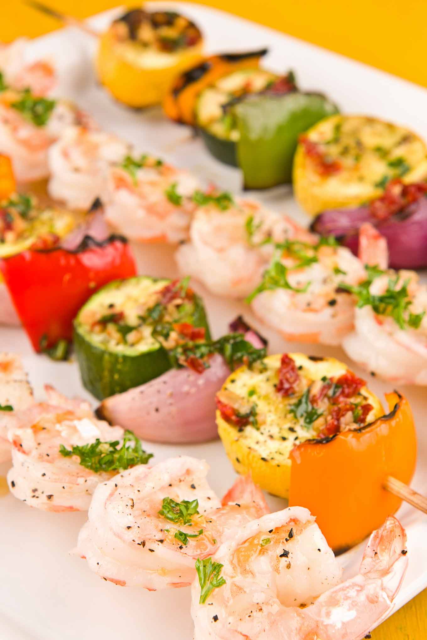 Close up photo of skewers of grilled shrimp and bell peppers, summer squash and red onion.