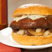 A side view of a balsamic glazed, grilled portobello mushroom on a soft hamburger bun with sautéed onions and creamy melted gorgonzola cheese.