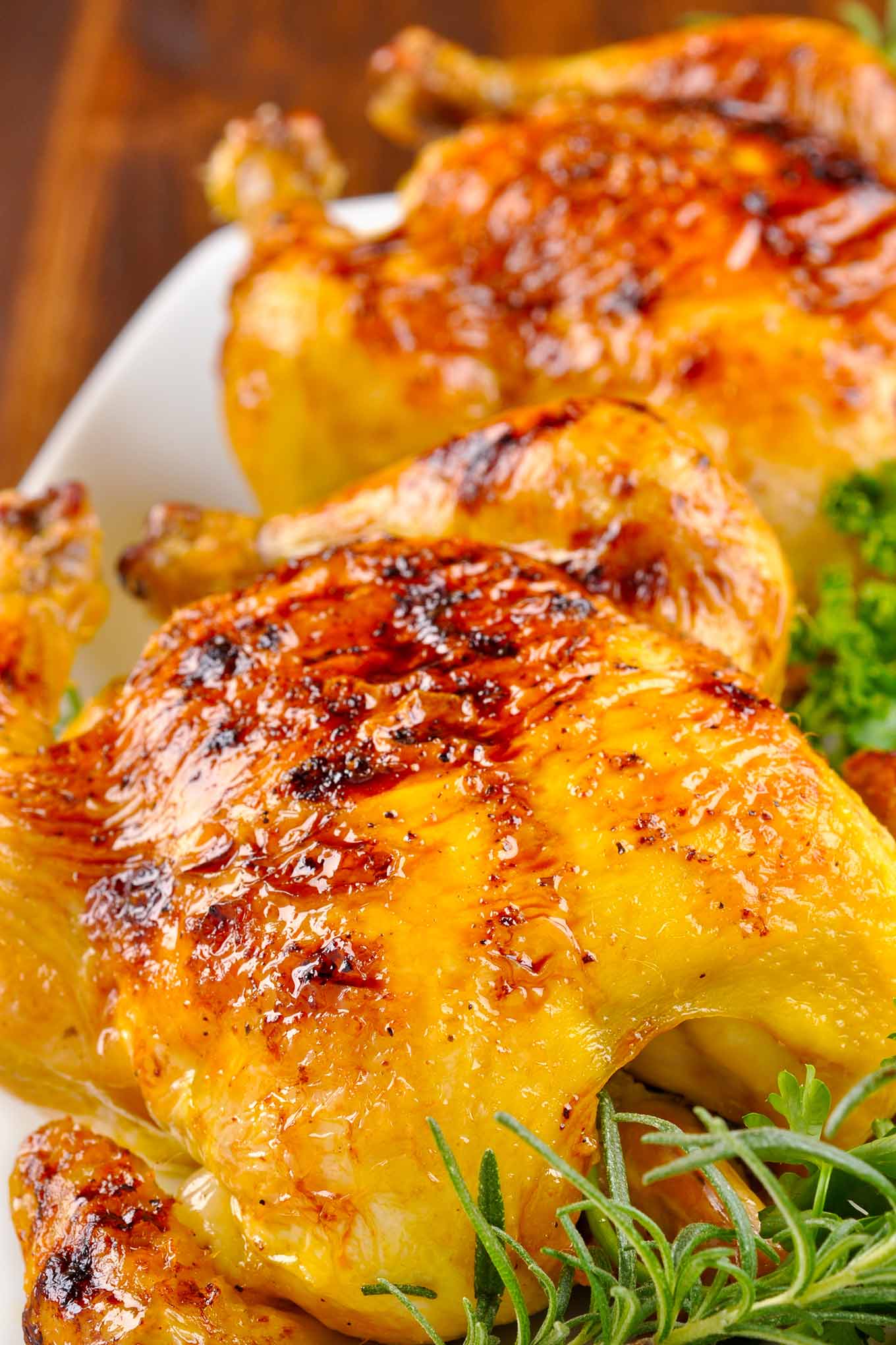Whole roasted Cornish game hens with bourbon glaze on a platter with herb garnish.
