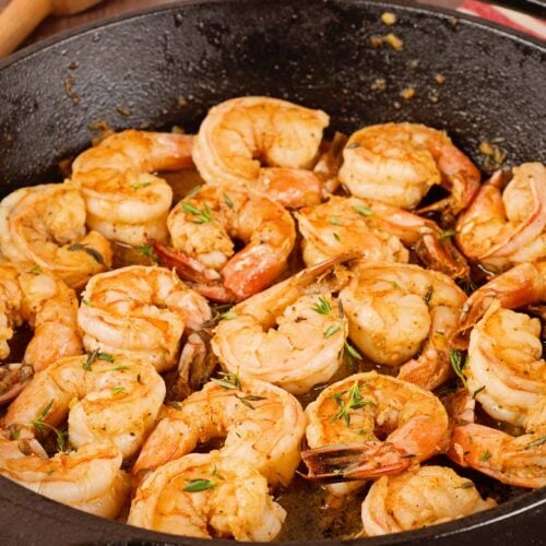 Sautéed shrimp in cast iron skillet seasoned with Old Bay Seasoning and garnished with fresh thyme leaves.