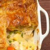 Pot pie baking dish with a single serving removed showing layers of flaky pastry and creamy chicken filling.