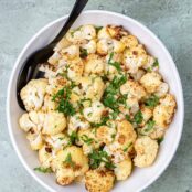 A serving bowl filled with oven-roasted cauliflower garnished with chopped parsley.