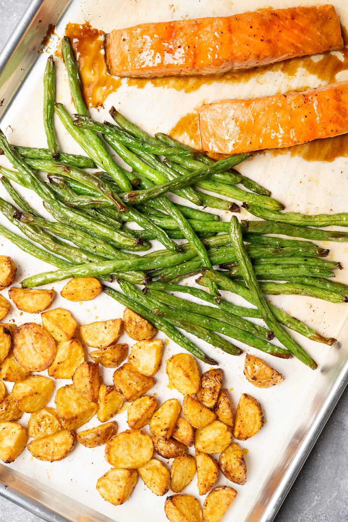 Oven-roasted salmon dinner on parchment-lined sheet pan: glazed salmon fillets, green beans, and potatoes.