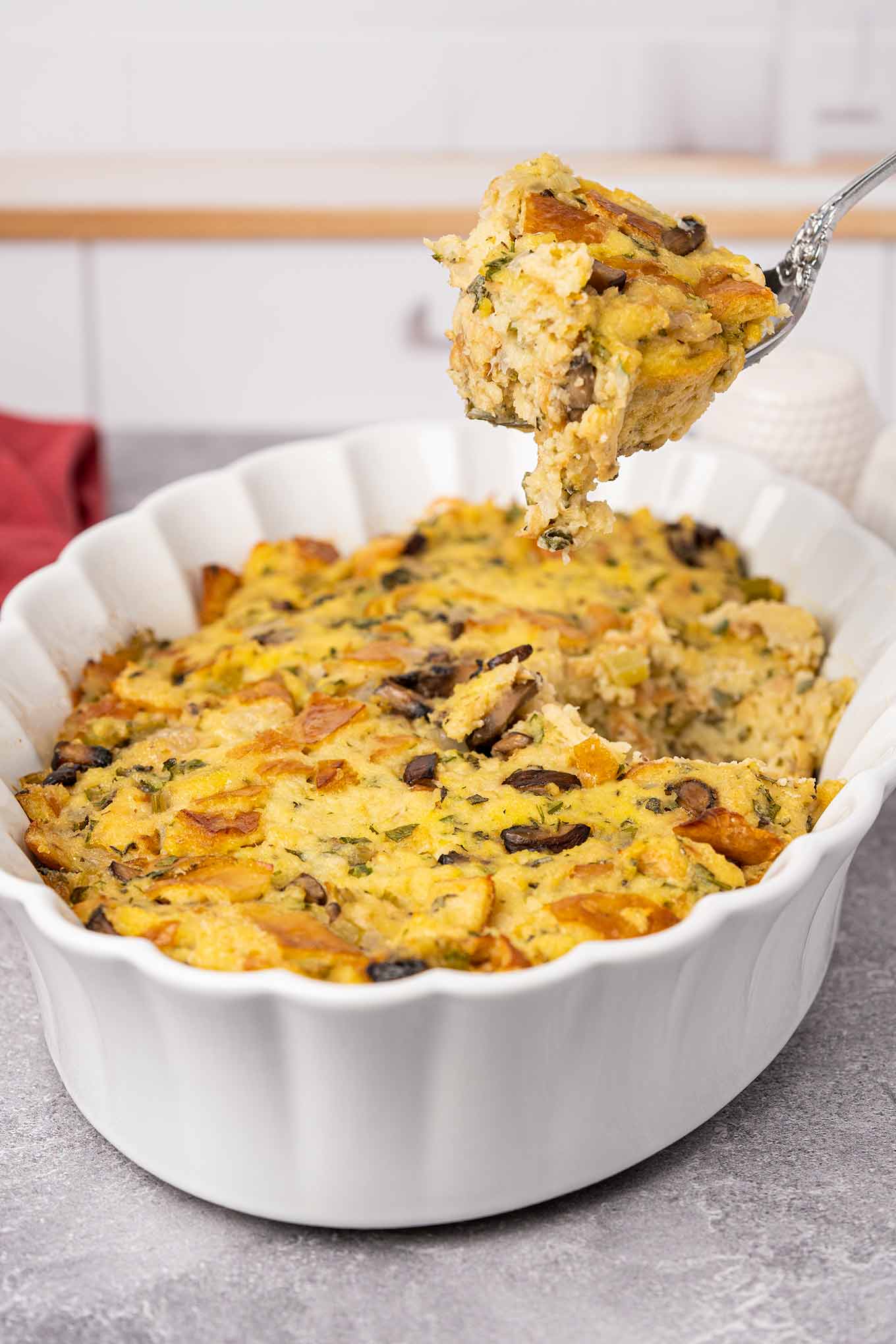 A casserole of traditional bread stuffing with a spoonful being removed for serving showing its moist, fluffy texture.