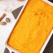 Baked casserole of fluffy whipped orange sweet potatoes with a fresh orange, cinnamon stick and nutmeg scattered on the side.