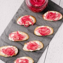 A slate serving board filled with blue cheese, mascarpone, and pickled onion crostini.