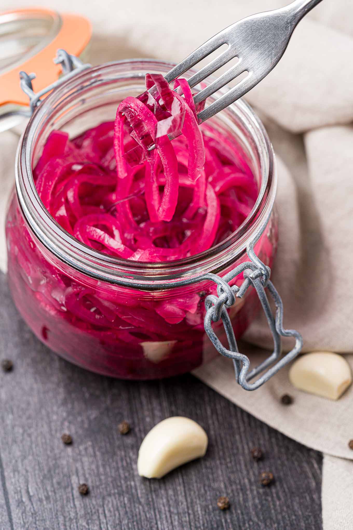 A forkful of pickled red onions being removed from an open canning jar. 