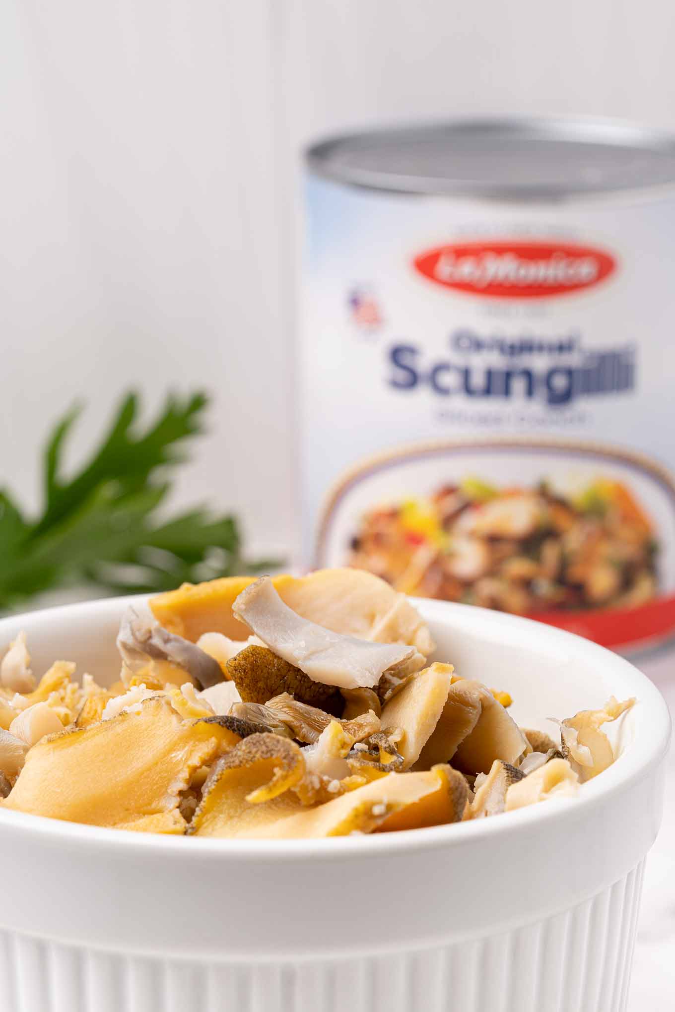 Closeup of a bowl of sliced scungilli with the can and some Italian parsley in the background.