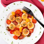 A serving dish of seared sea scallops and roasted grape tomatoes topped with shallot-butter sauce.