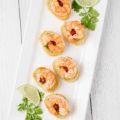 A serving platter filled with shrimp and avocado crostini and garnished with cilantro and lime.