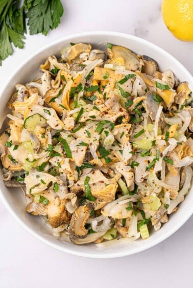 Serving bowl filled with snail (scungilli) salad with celery, onion, parsley, and crushed red pepper.