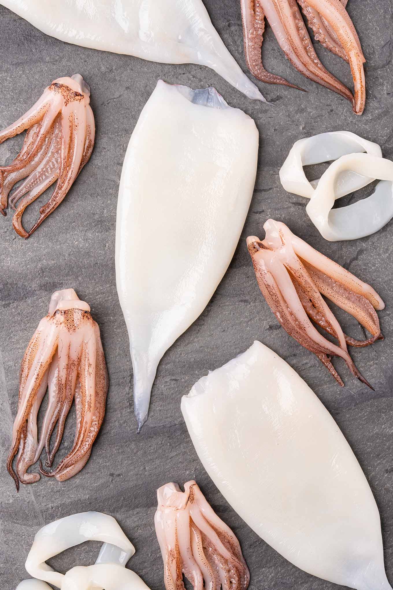 Overhead view of calamari (squid) tubes, tentacles, and rings on a black slate board.