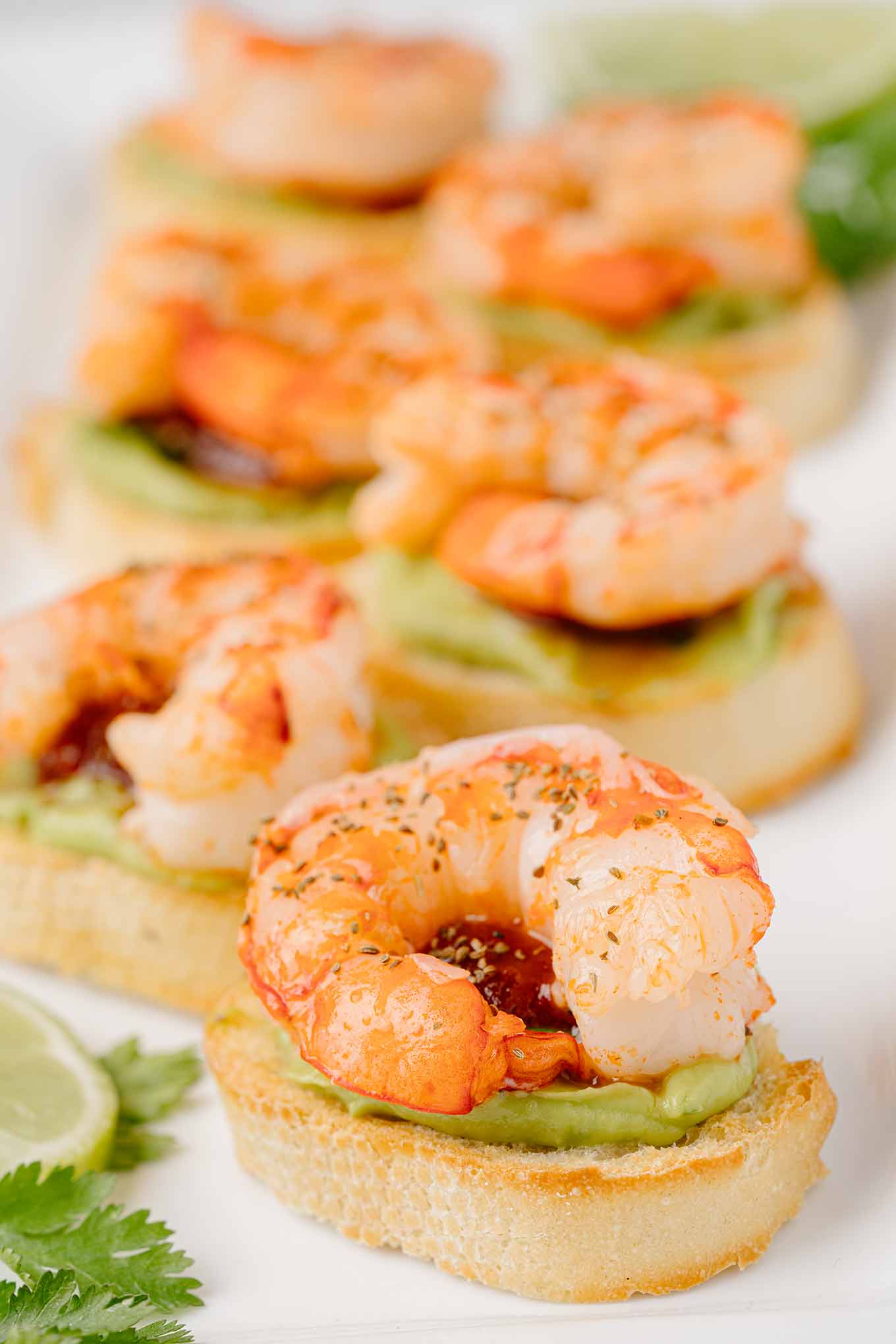 Close up side view of shrimp appetizer showing crostini and layers of avocado puree, cilantro, chili sauce, shrimp, and celery seed.