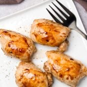 A square serving plate containing four boneless, skinless chicken thighs, roasted and glazed with honey and balsamic vinegar.
