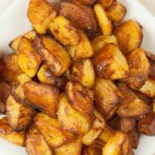 Crispy, golden brown, oven roasted potatoes on a white serving plate.