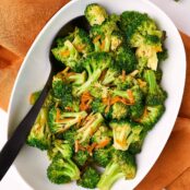 Sauteed broccoli with citrusy orange peel, presented in a white oval bowl and accompanied by a black serving spoon.