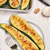 A white plate and fork with two zucchini halves filled with a golden brown mixture of sautéed vegetables, cheese and crispy breadcrumbs.