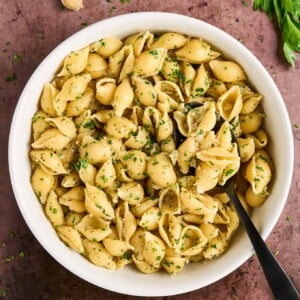 White bowl filled with cooked pasta shells tossed in garlic butter with balsamic vinegar, garnished with chopped parsley.
