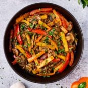Sautéed peppers, mushrooms and onions with a sprinkle of fresh chopped parsley, served in a black ceramic bowl.