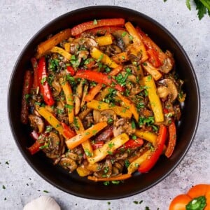 Saut&eacute;ed peppers, mushrooms and onions with a sprinkle of fresh chopped parsley, served in a black ceramic bowl.