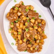 An oval serving platter of Caribbean-style pineapple pork with tender pork medallions, pineapple chunks, and scallions in a sweet-savory rum sauce.