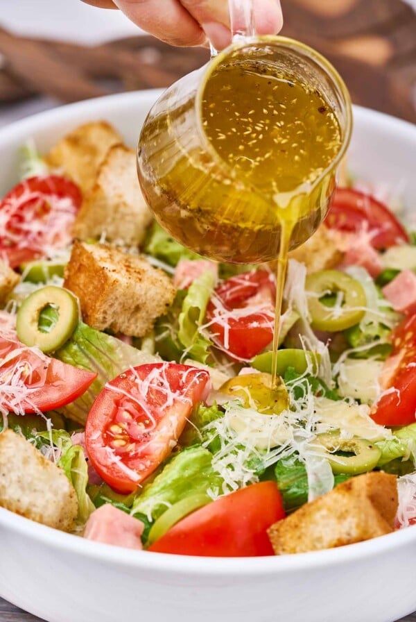 1905 salad with ham, olives, tomatoes, Parmesan cheese, croutons, and garlic dressing being poured over the salad