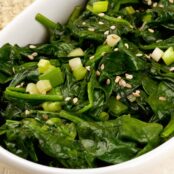 An oval serving dish filled with fresh spinach, scallions, and sesame seeds sautéed in sesame oil.