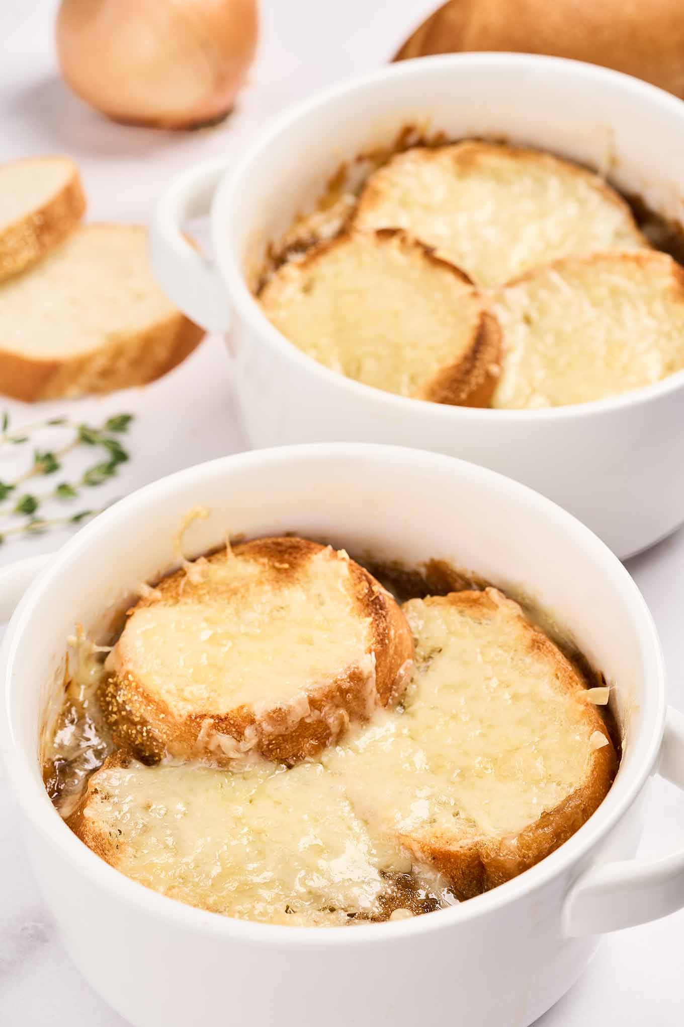 A close up view of French onion soup in round white crocks with handles.