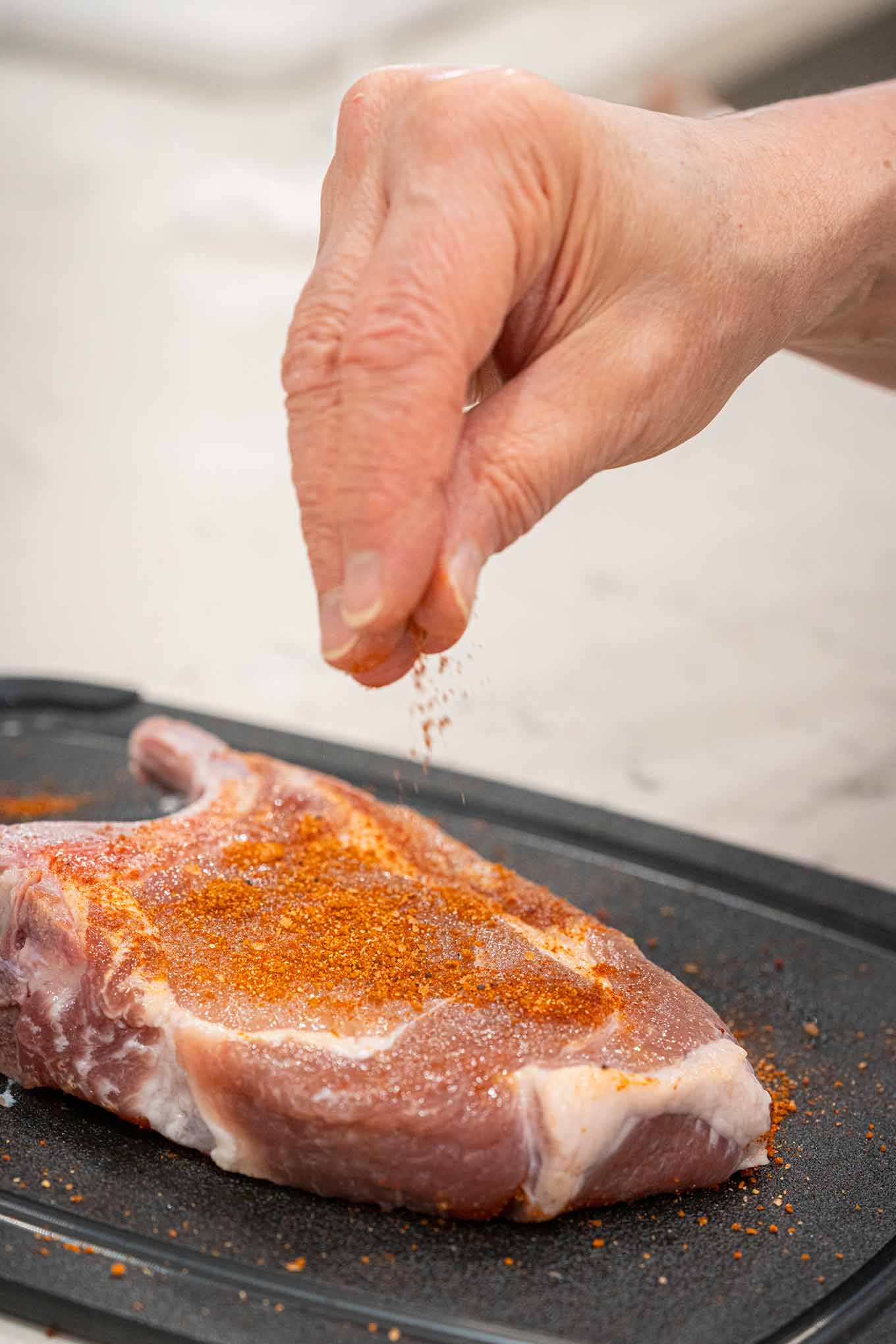 BBQ spice rub being sprinkled onto pork chops showing how to get even distribution of the rub on meat.
