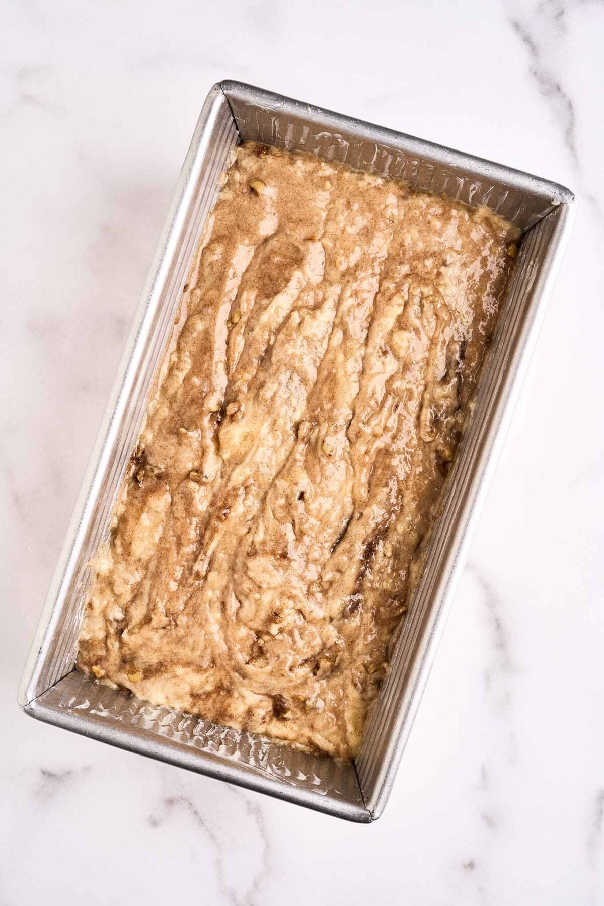 A corrugated loaf pan filled with cinnamon walnut quick bread batter, ready for the oven.