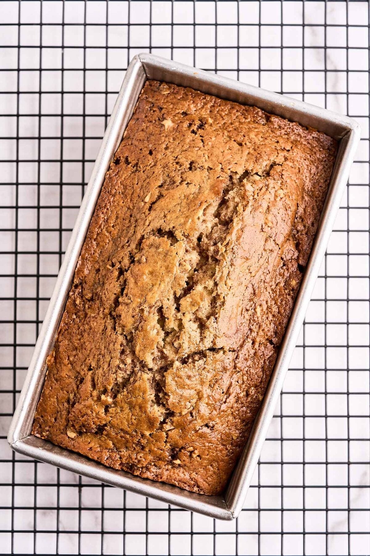 An overhead view of cinnamon walnut quick bread cooling in its pan on top of a black wire cooling rack.