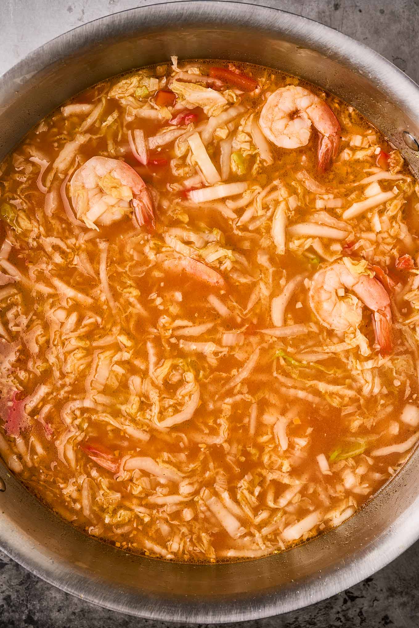 An overhead view of ramen broth combined with napa cabbage, bell peppers, and shrimp.