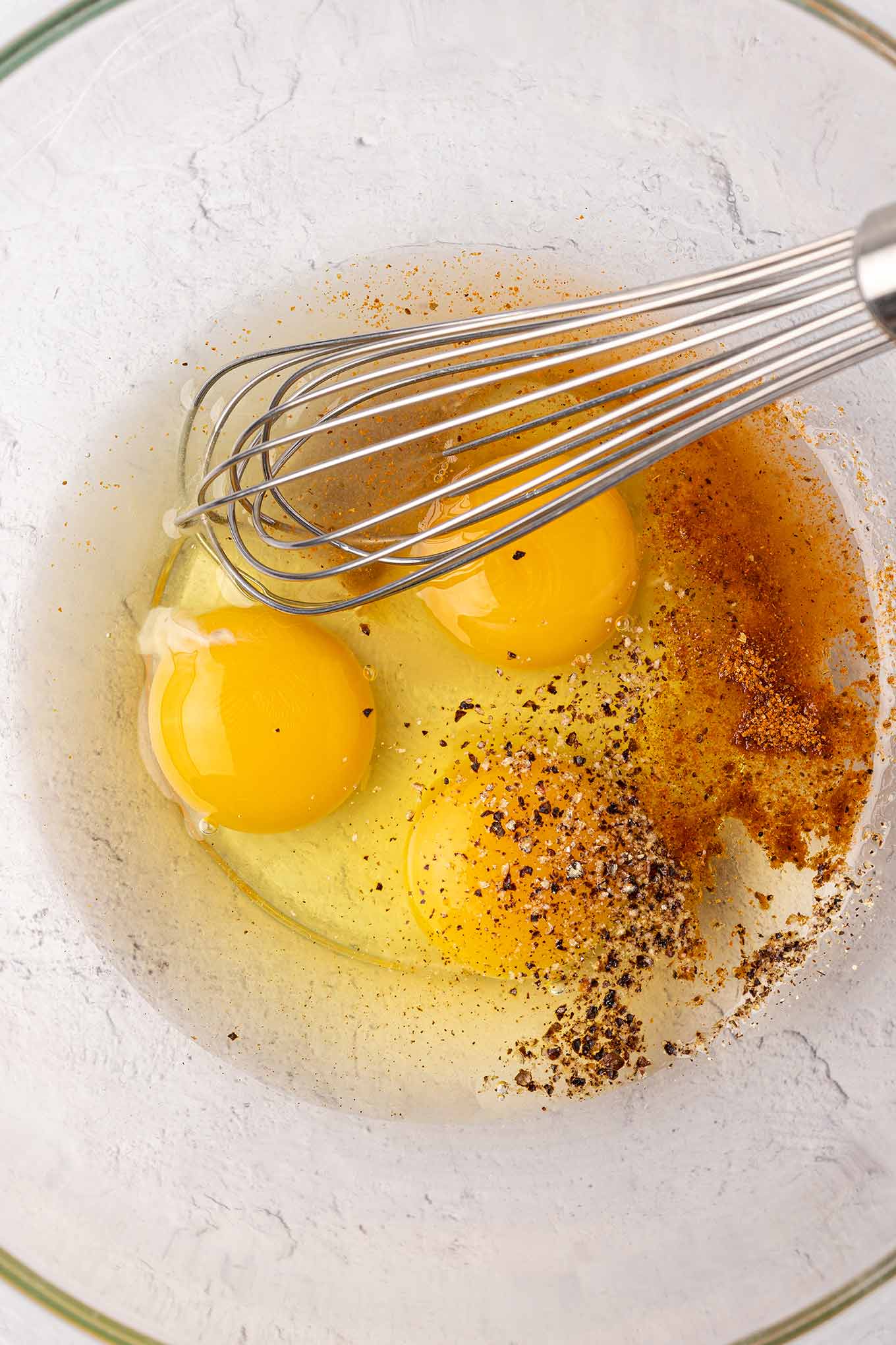 The wet ingredients for making crab cakes; eggs, lemon juice, Old Bay seasoning, and mayo in a mixing bowl with a whisk.