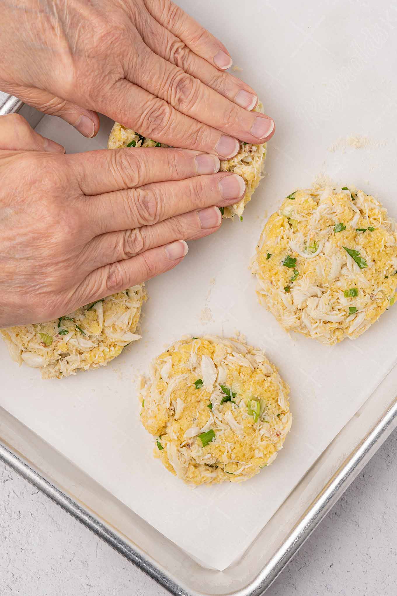 Crab cakes being formed on a baking sheet, being prepared to go into the oven.