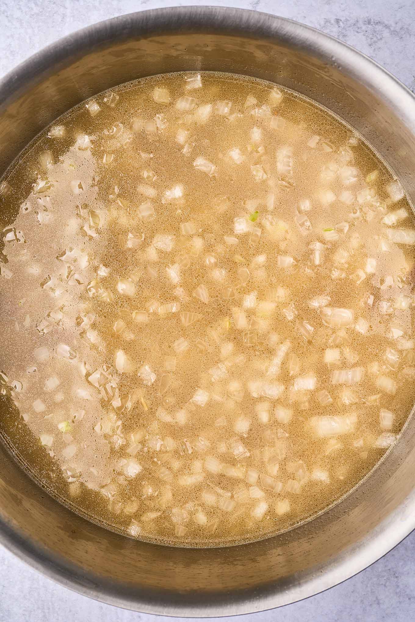Preparing corn chowder; a soup pot with potatoes simmering in chicken broth flavored with sautéed onion and garlic.