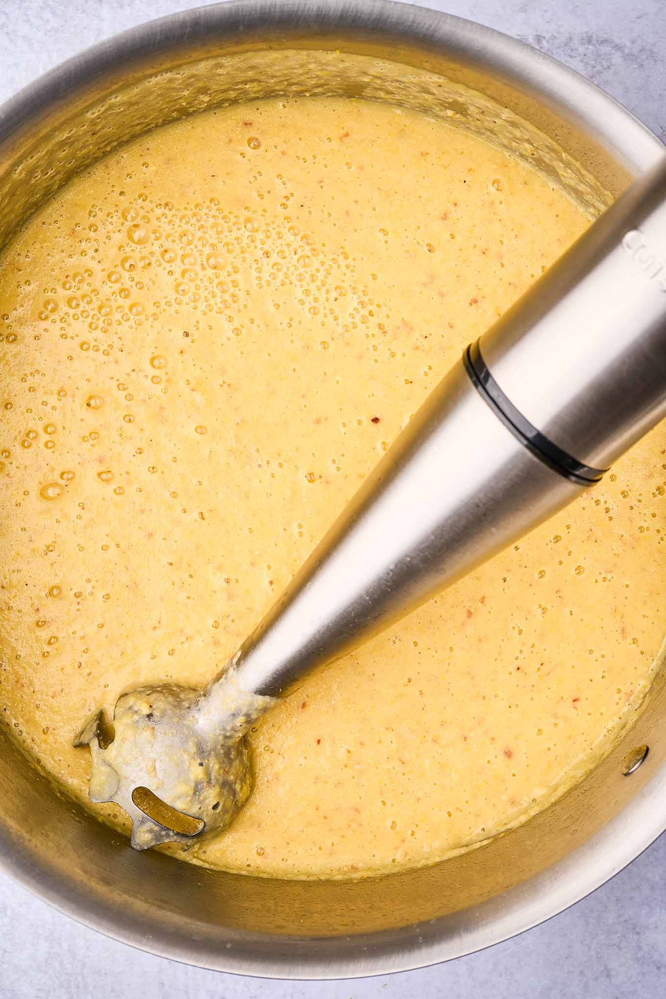 A soup pot of corn chowder being pureed with an immersion blender.