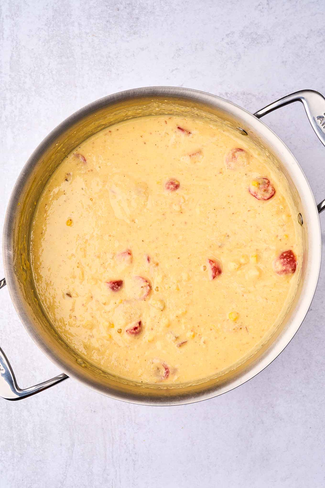 A soup pot filled with pureed corn chowder, chunks of potatoes, fresh tomatoes, corn kernels, and bacon returned to the pan for texture.