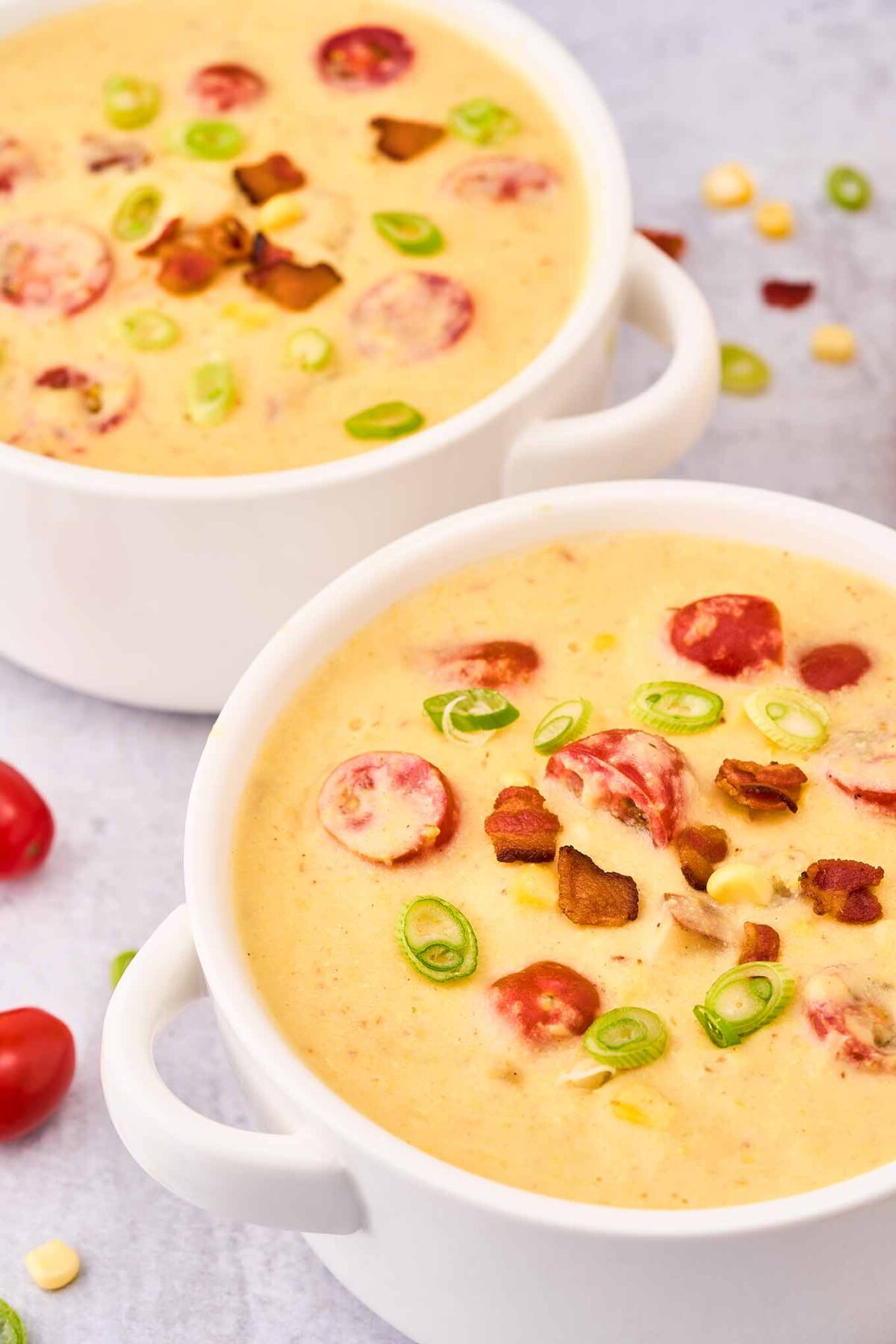 A single serving bowl of creamy corn chowder with bacon and tomato, a second bowl in the background.