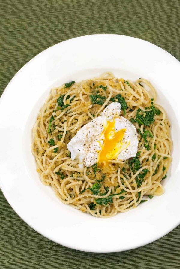 A plate of spaghetti tossed with toasted garlic breadcrumbs and fresh spinach, topped with a poached egg.